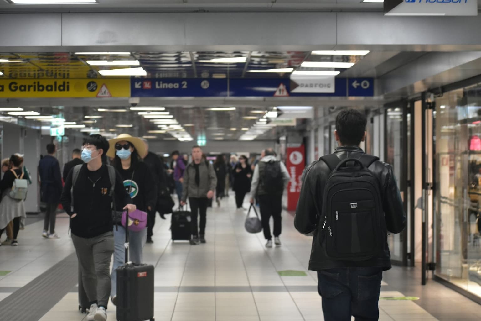 A busy corridor at Rome's Termini/Garibaldi station, travelers walking with rolling suitcases and backpacks past the station signage
