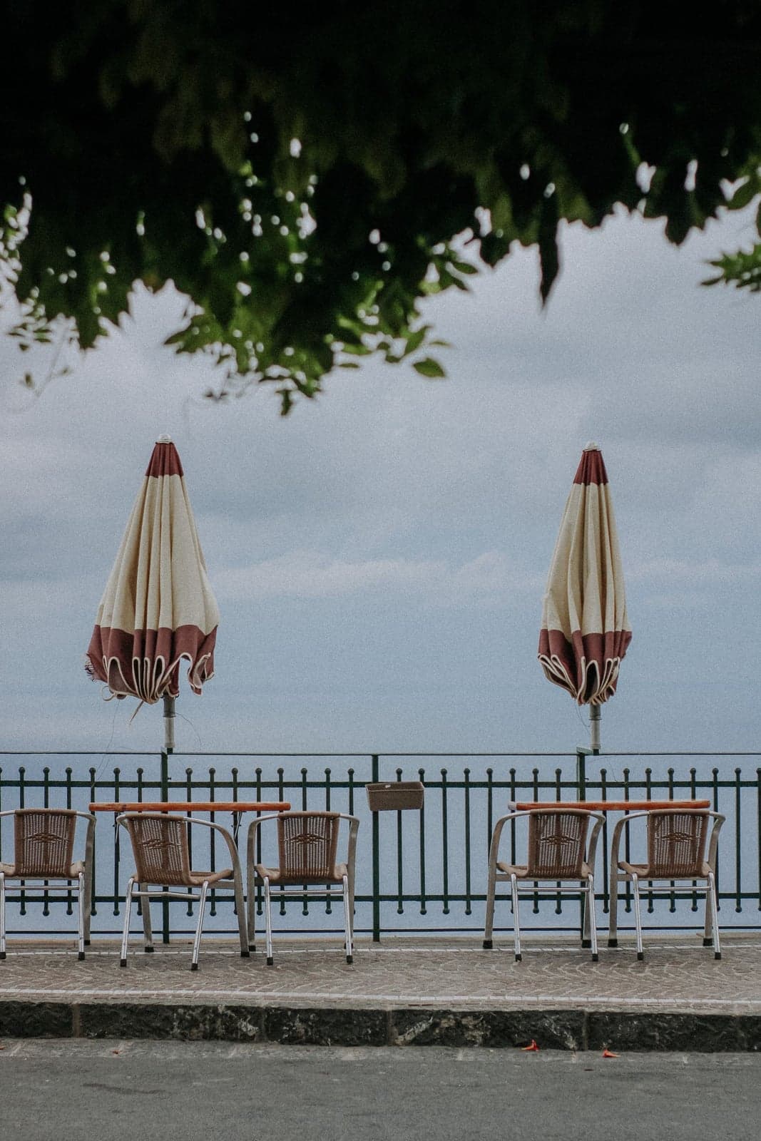 A row of closed beach chairs and furled umbrellas along a seaside railing, the beach club behind them shut for the season