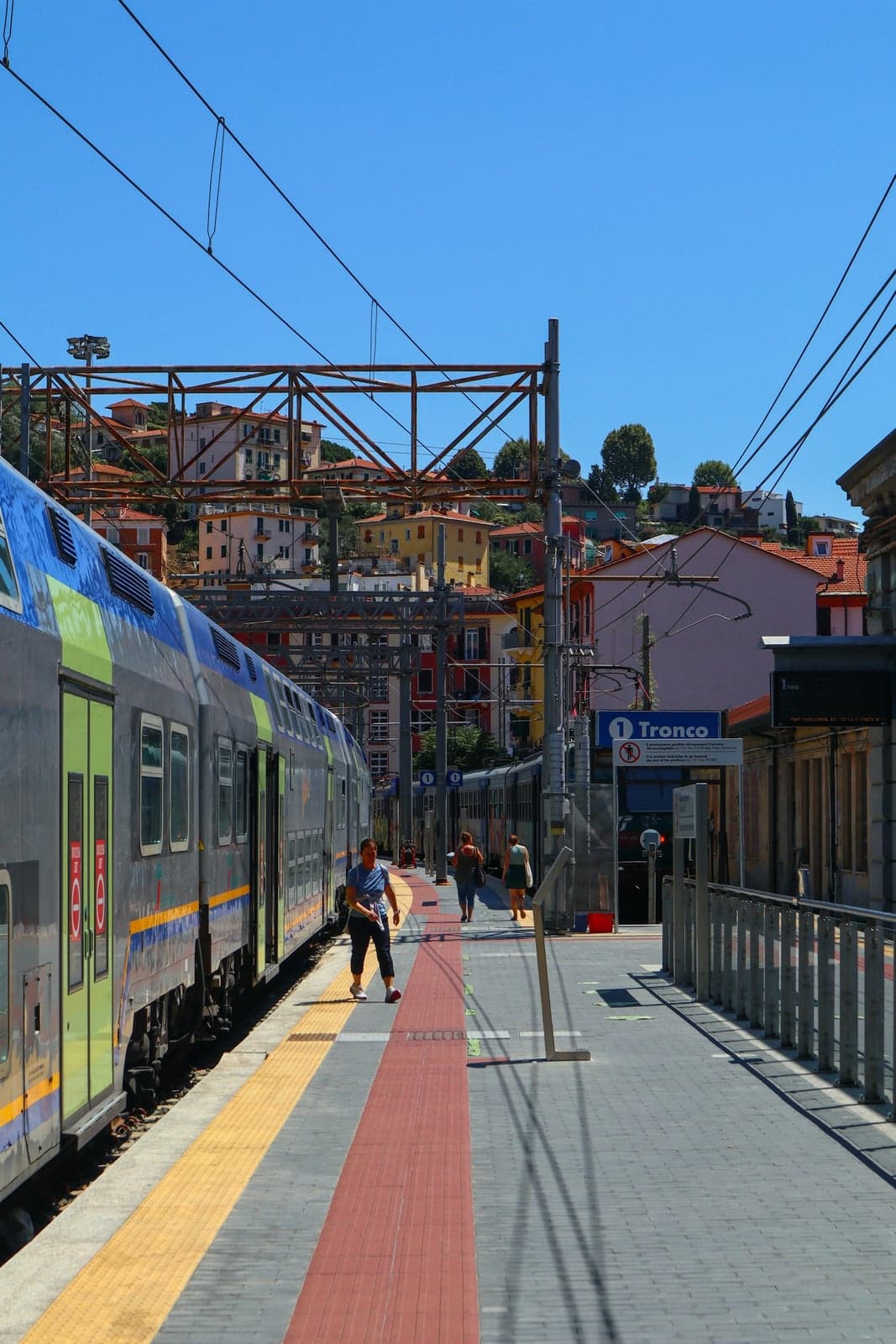 A regional train at the platform of La Spezia Centrale, with the hillside town's pastel houses rising behind the station.