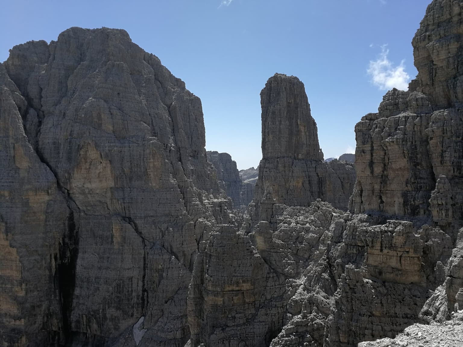 The free-standing shaft of Campanile Basso rising between sheer, banded rock walls in the Brenta group