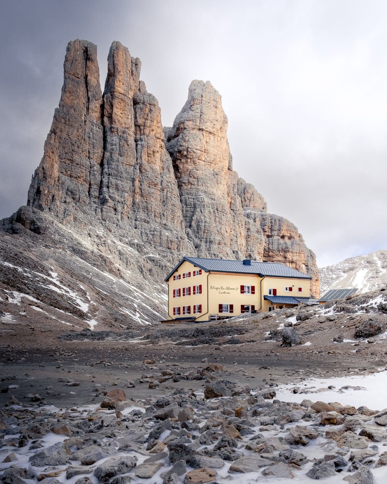 The Torri di Vajolet rising straight above Rifugio Re Alberto I, a yellow hut with red shutters, on rock and scree dusted with fresh snow