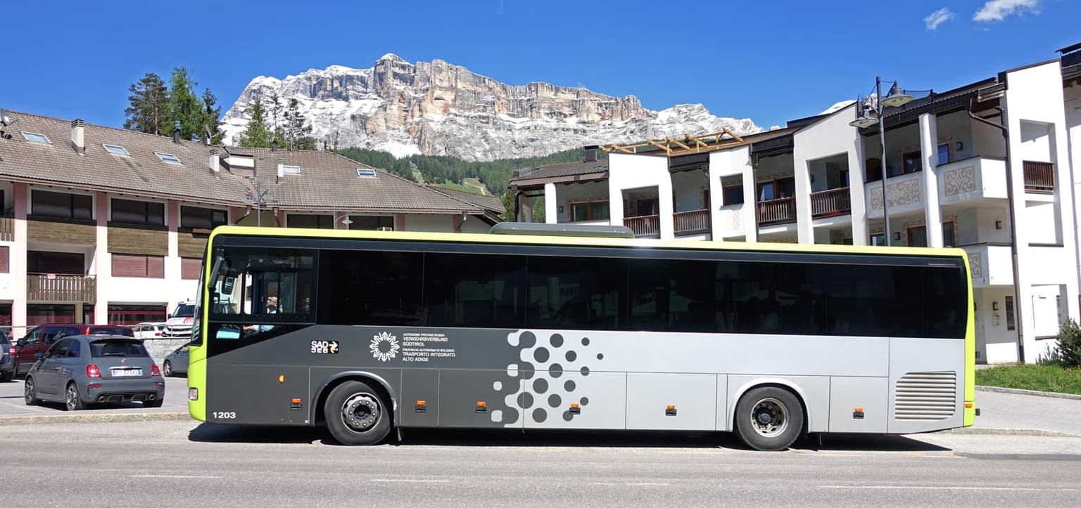 A South Tyrol regional bus in Alta Badia, branded with the province's own Verkehrsverbund Südtirol transit network, dolomite rock walls rising behind it
