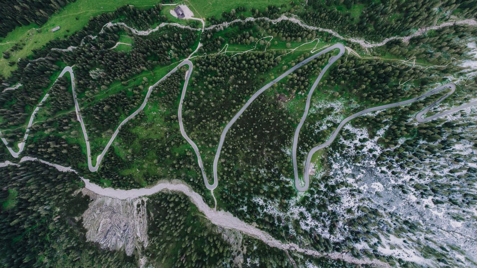 Aerial view of the hairpin switchbacks on the road to Passo Gardena, the pavement doubling back on itself up the forested slope
