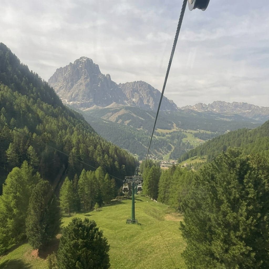 The Col Raiser gondola climbing above Santa Cristina, looking back down over the forested valley and village below as the cabin ascends.