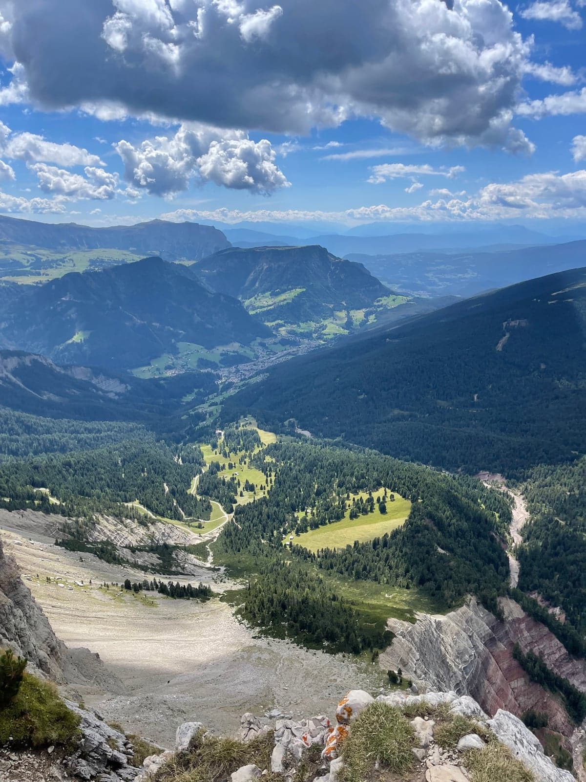 A high view from the Seceda viewpoint down over Val Gardena toward Ortisei, forested slopes falling away to the village far below.