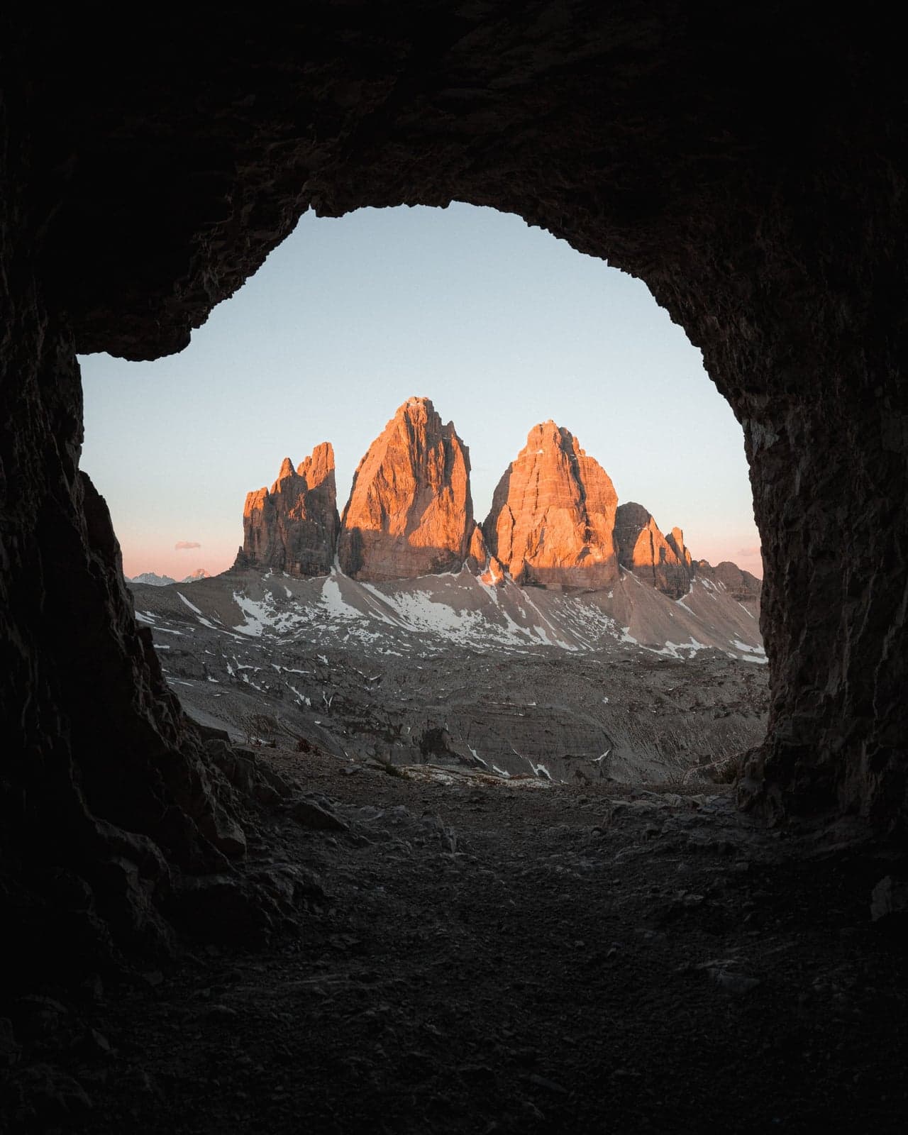 A WWI-era rock-window bunker at Sasso di Sesto frames the three peaks of Tre Cime di Lavaredo through the opening, warm sunset light on the towers, no crowd in sight.