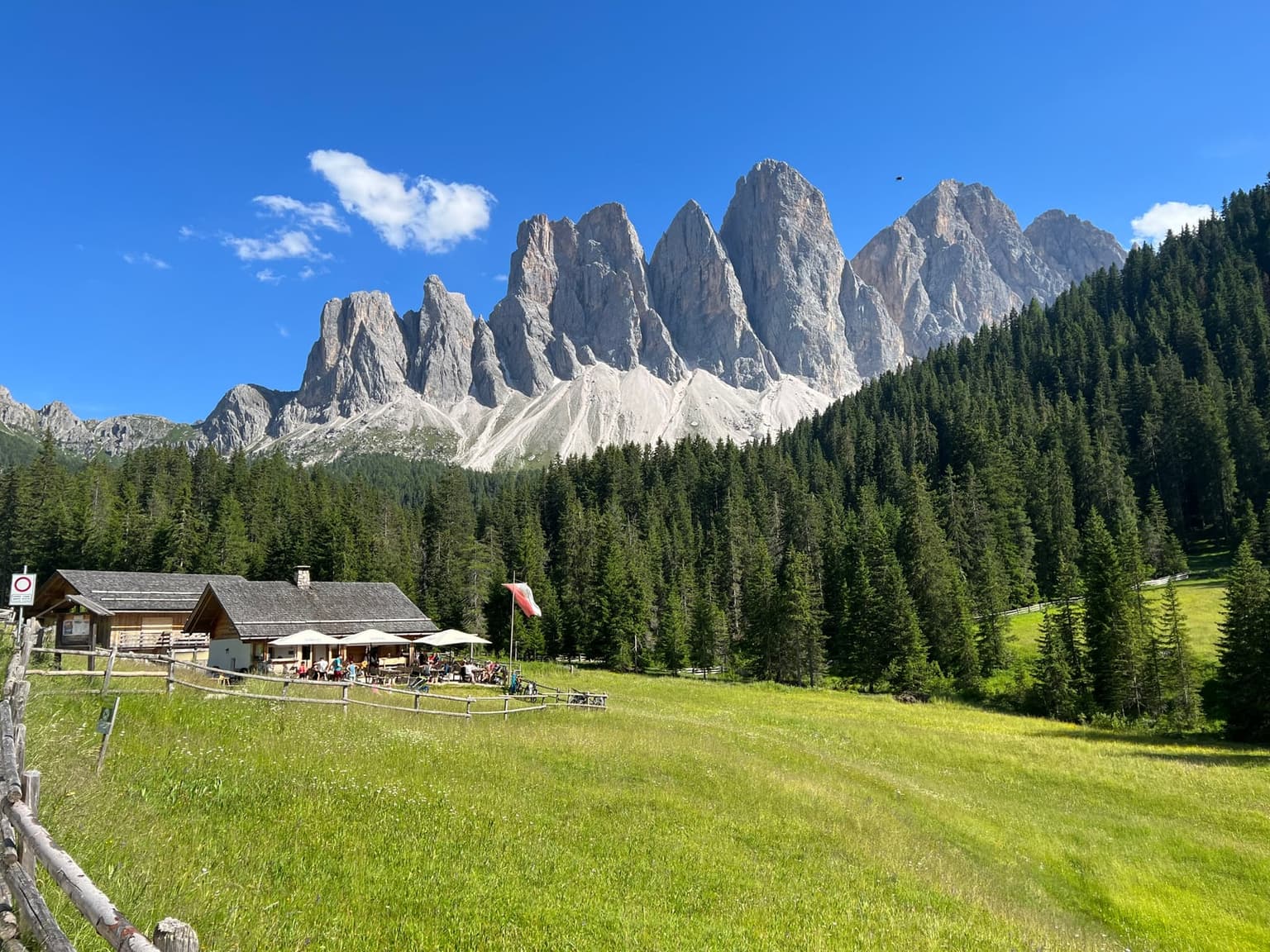 Rifugio Malga Brogles, a mountain hut with an outdoor terrace, below the jagged wall of the Odle