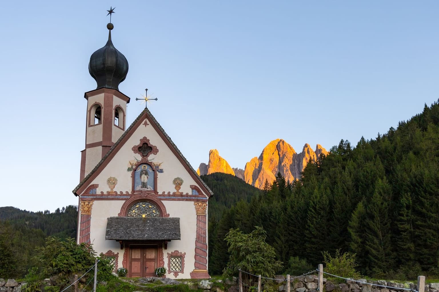 The chapel of San Giovanni in Ranui in its walled meadow, with the north faces of the Odle rising behind it