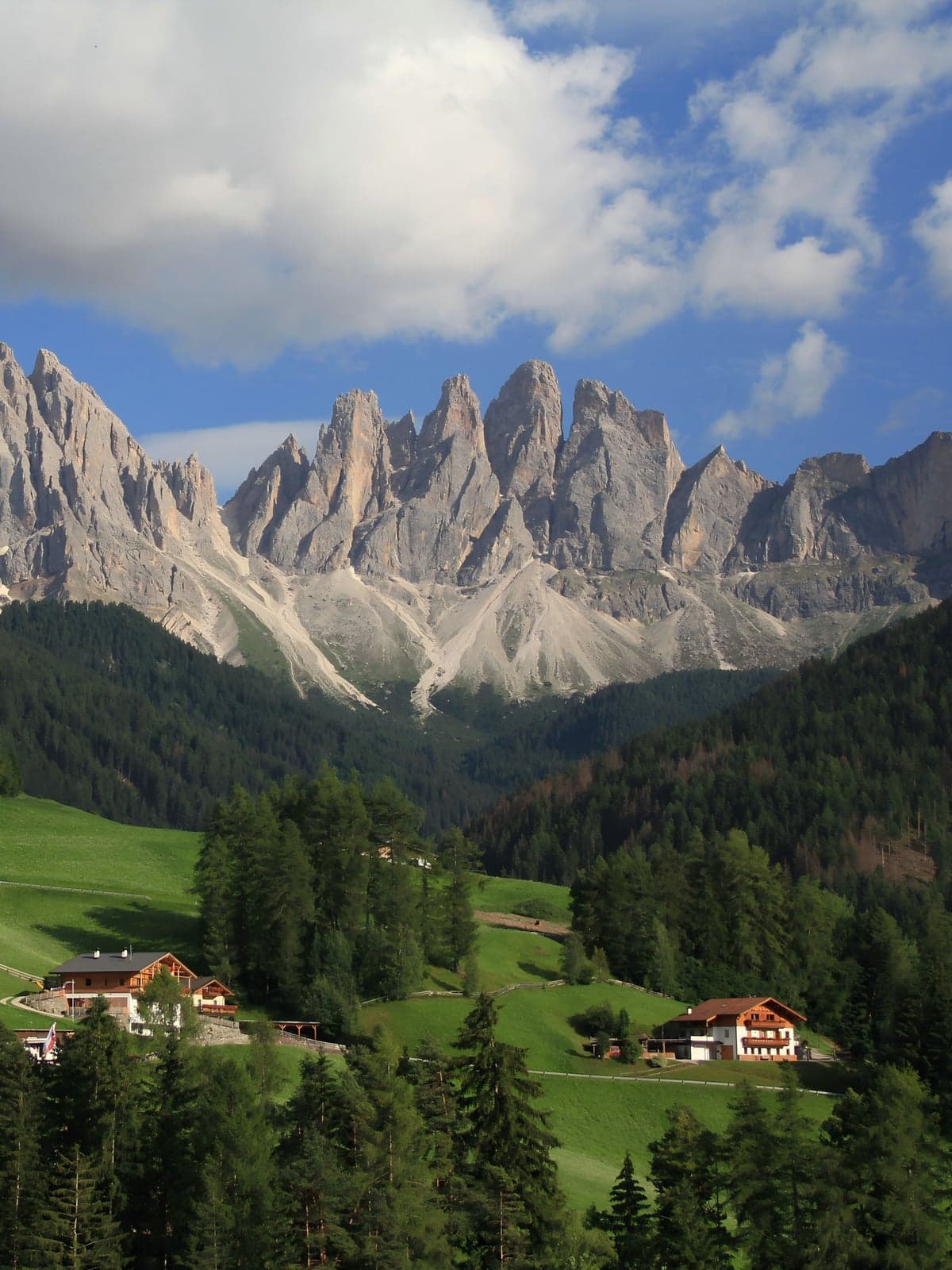 Val di Funes seen from above, green meadows and farmhouses scattered below the jagged wall of the Odle