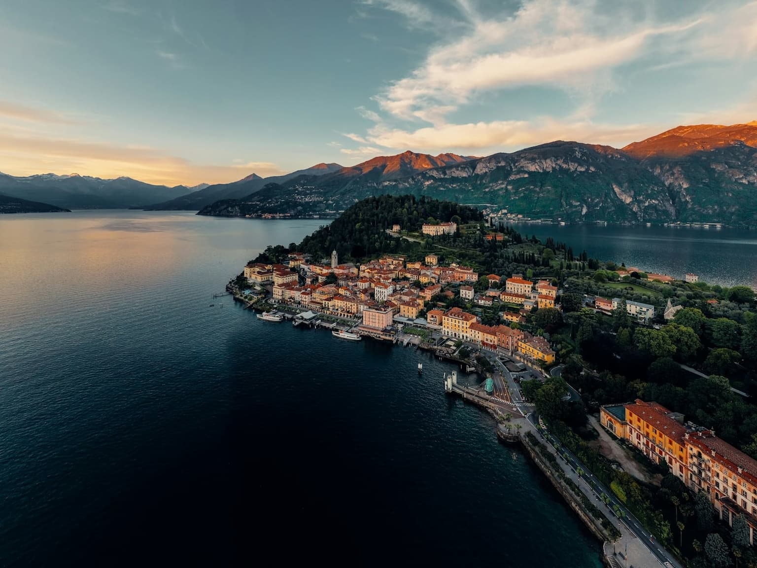 Aerial view of the Bellagio peninsula at sunset, the town on the point where Lake Como divides around the promontory, mountains glowing behind