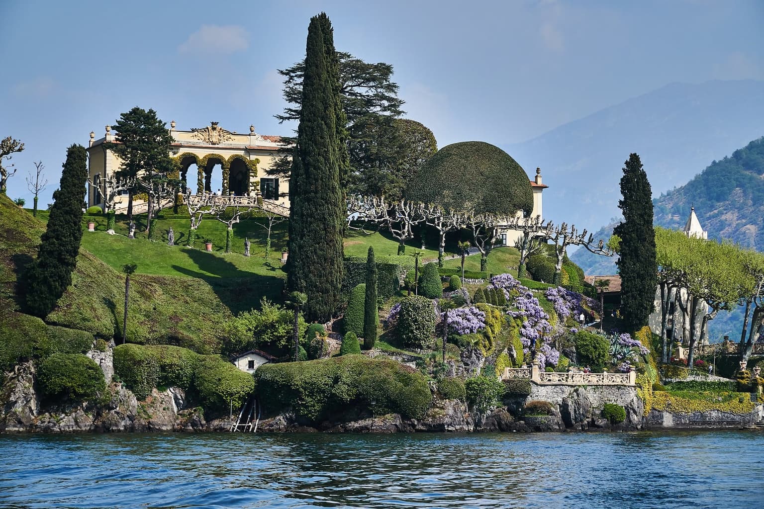 Villa del Balbianello seen from the water, its arched loggia and terraced gardens on a wooded promontory over Lake Como
