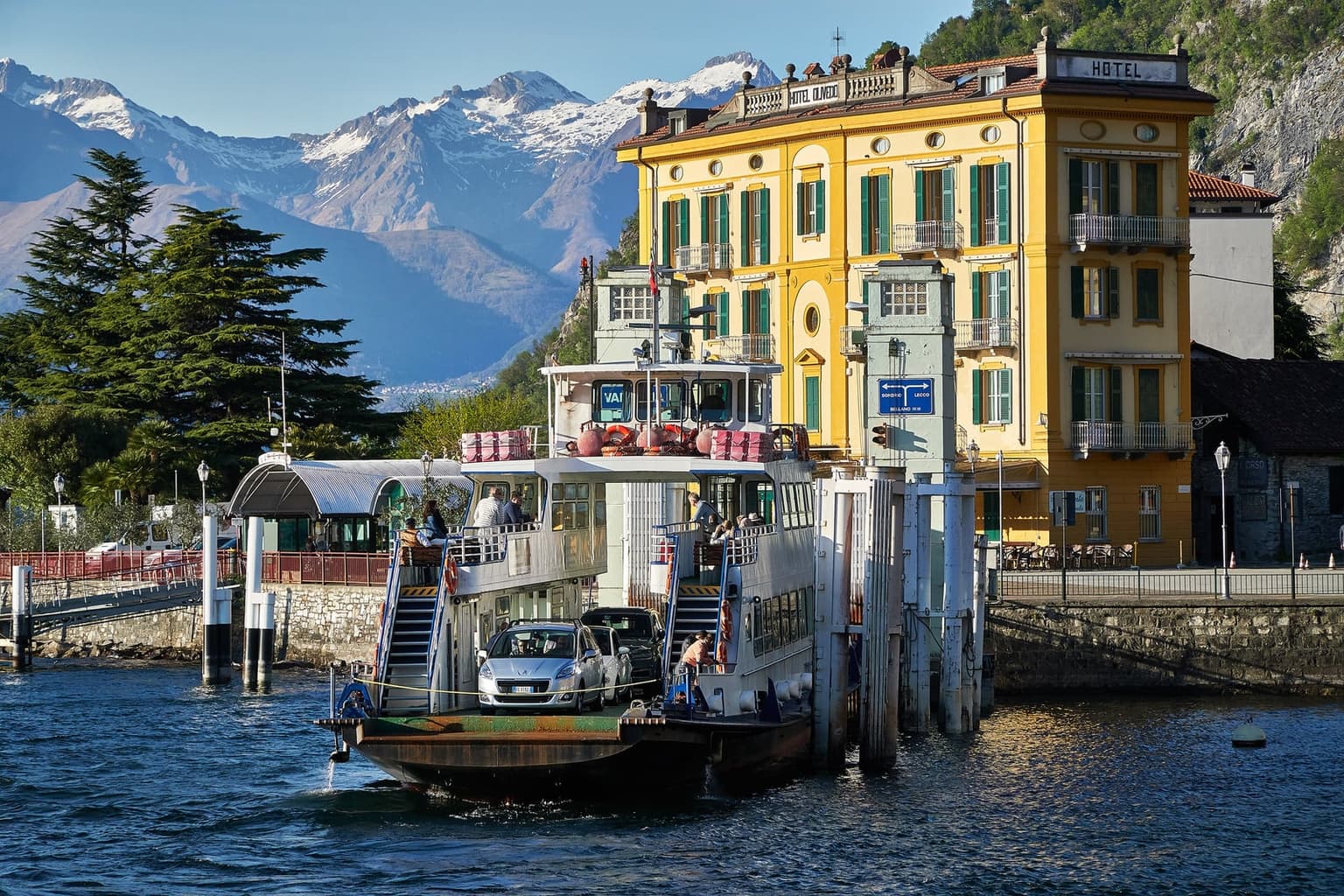 A Lake Como traghetto car ferry loading a car at the Bellagio dock, the yellow Hotel Metropole rising behind