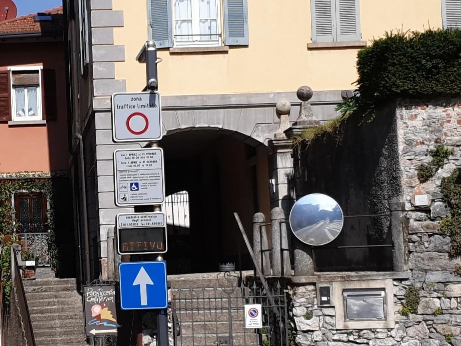 A zona traffico limitato (ZTL) sign at a pedestrian-zone entrance in Bellagio, with its enforcement camera above and a green ATTIVO indicator showing the zone is live