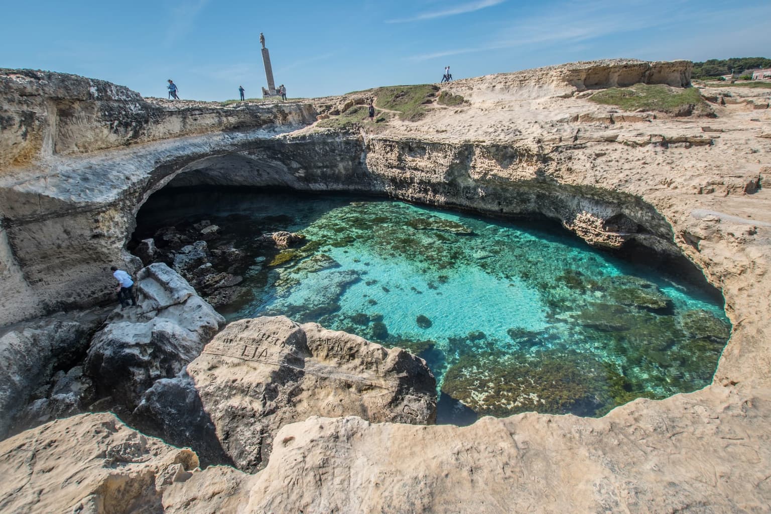 The Grotta della Poesia near Roca Vecchia seen from its rim: a round sinkhole of turquoise water open to the sea through an arch