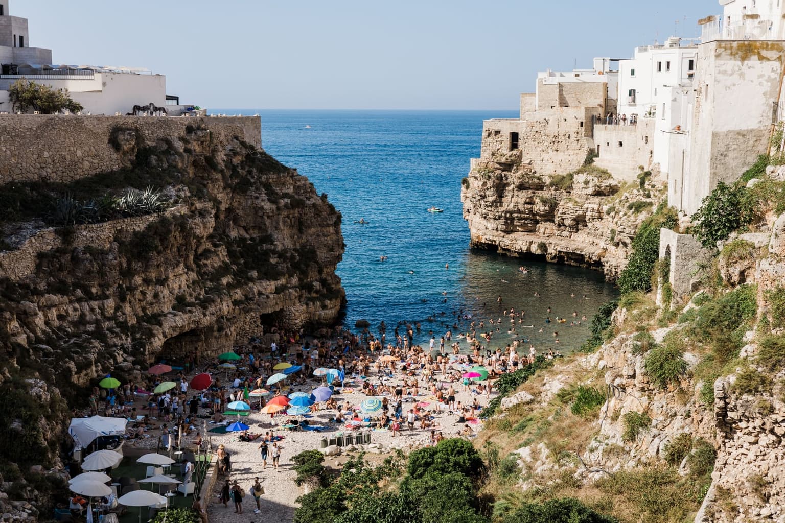 Lama Monachile, the pebble cove at Polignano a Mare between white limestone walls, with swimmers in the water and houses at the cliff edge