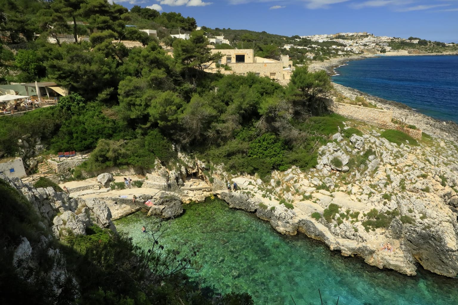 A rock platform at Cala dell'Acquaviva with swimmers in clear, deep water and no sand beach in sight