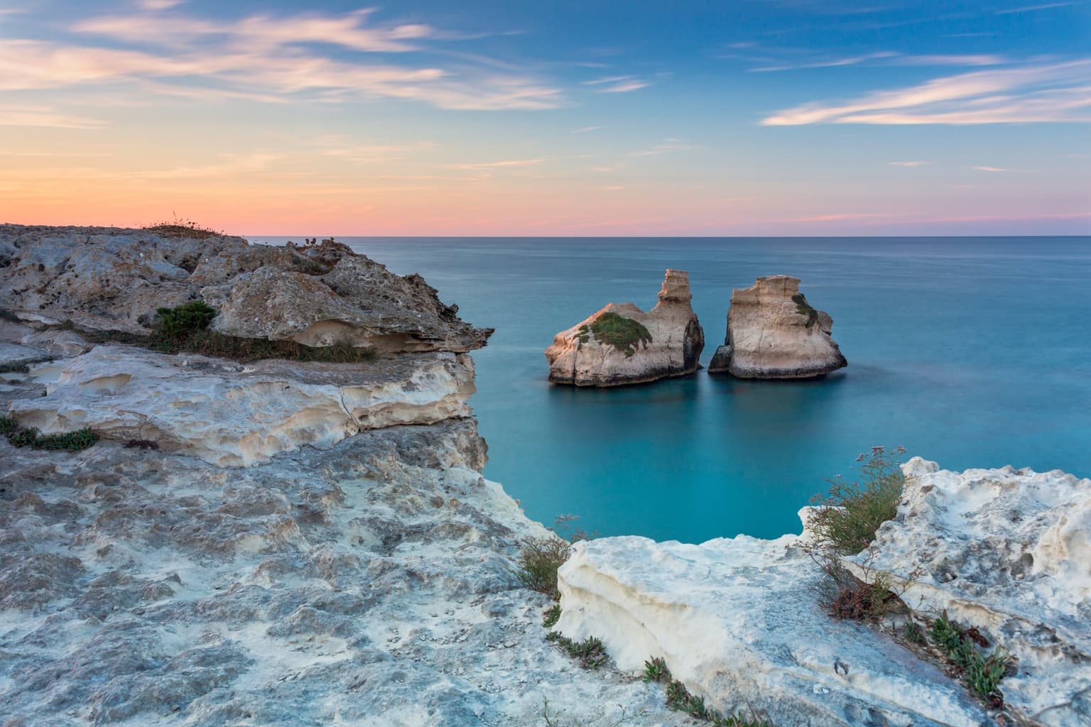 The Due Sorelle stacks rising from calm water at Torre dell'Orso, seen from the cliff top at dusk