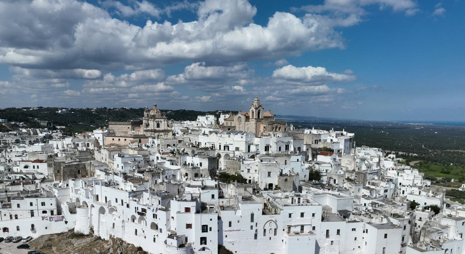 Ostuni's old town from the air, white houses packed on its hill above the round bastions of the walls, the cathedral at the top and olive groves running out toward the sea