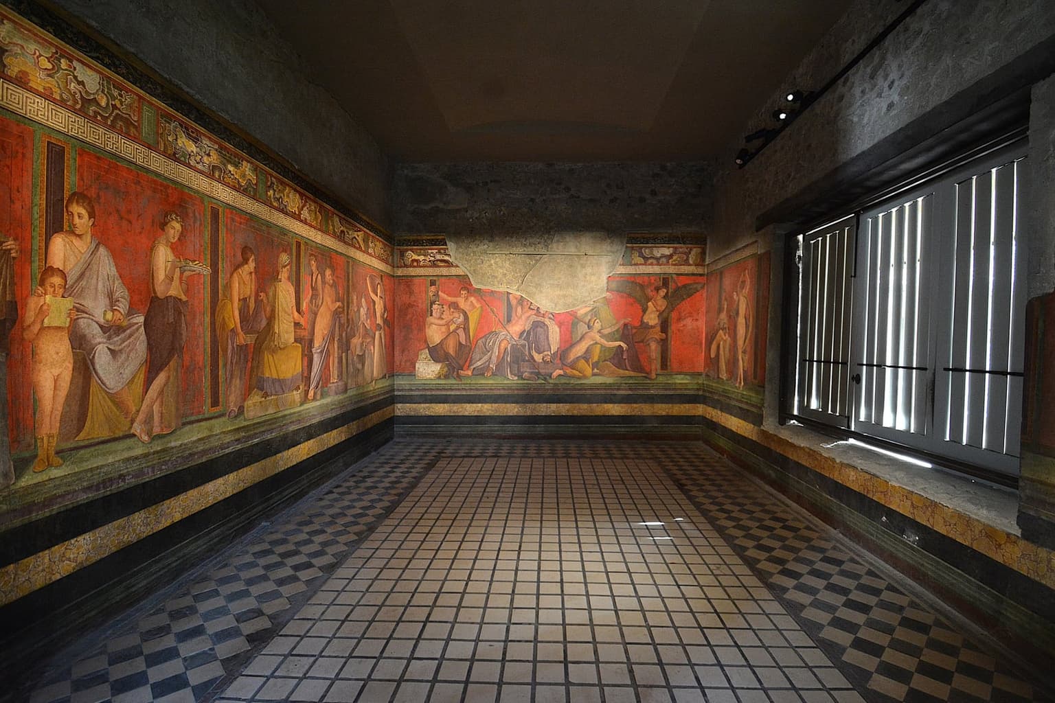The painted room of the Villa of the Mysteries at Pompeii, its walls covered in a continuous red fresco of life-size figures above a black-and-white checkered floor