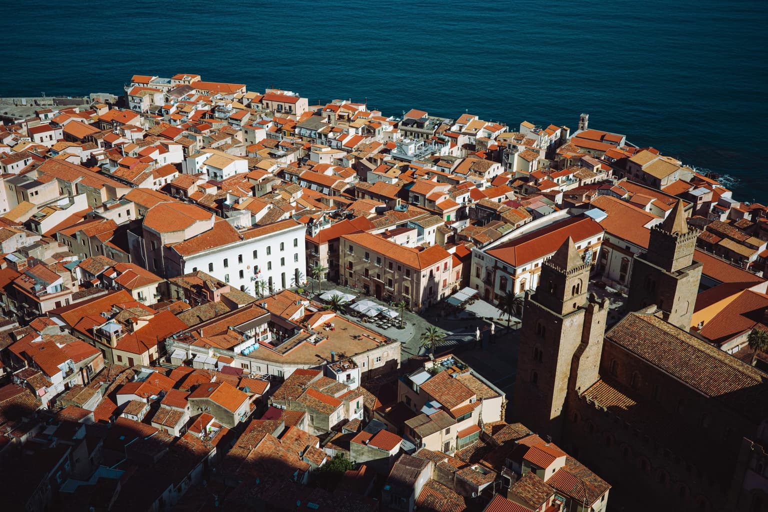 Looking down on Cefalù from La Rocca, the cathedral's towers and Piazza Duomo among terracotta roofs that run out to the sea