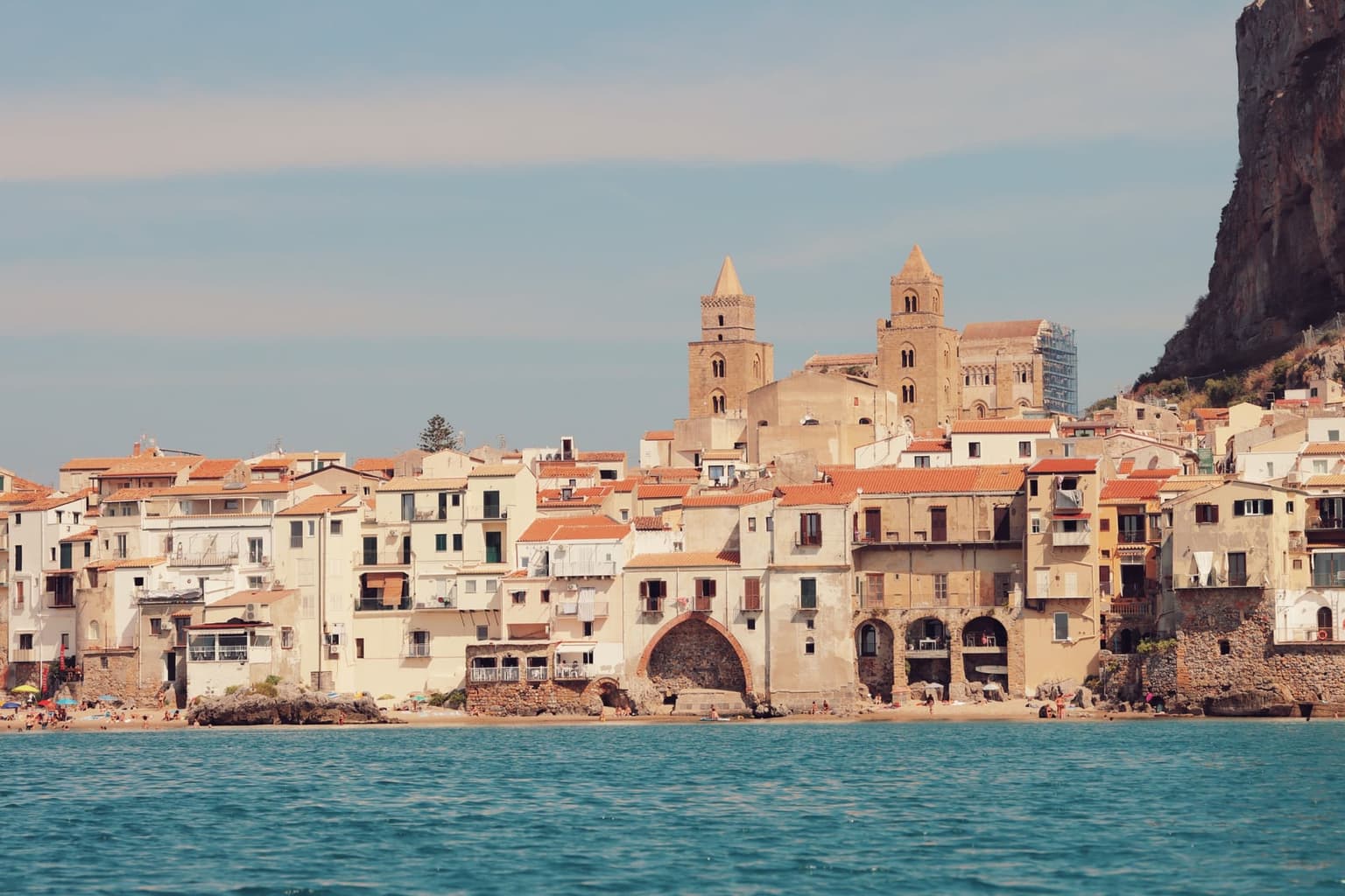 Cefalù from the sea, the cathedral's two towers rising over the waterfront houses with the cliff of La Rocca at the right edge
