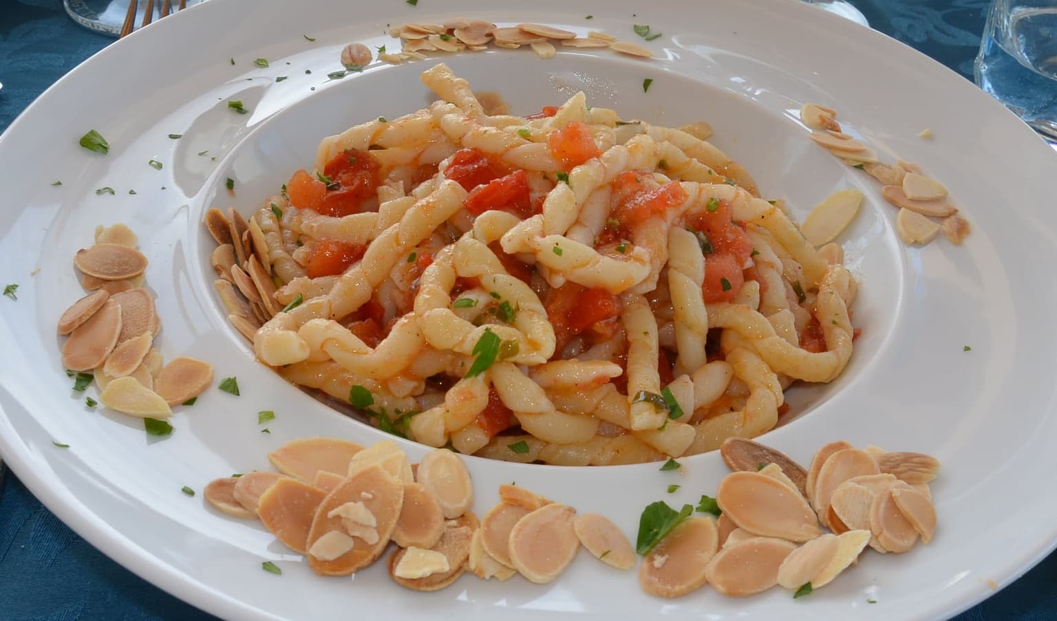 A plate of busiate, Sicily's thick hand-rolled corkscrew pasta, tossed with fresh tomato and basil and ringed with toasted almond flakes