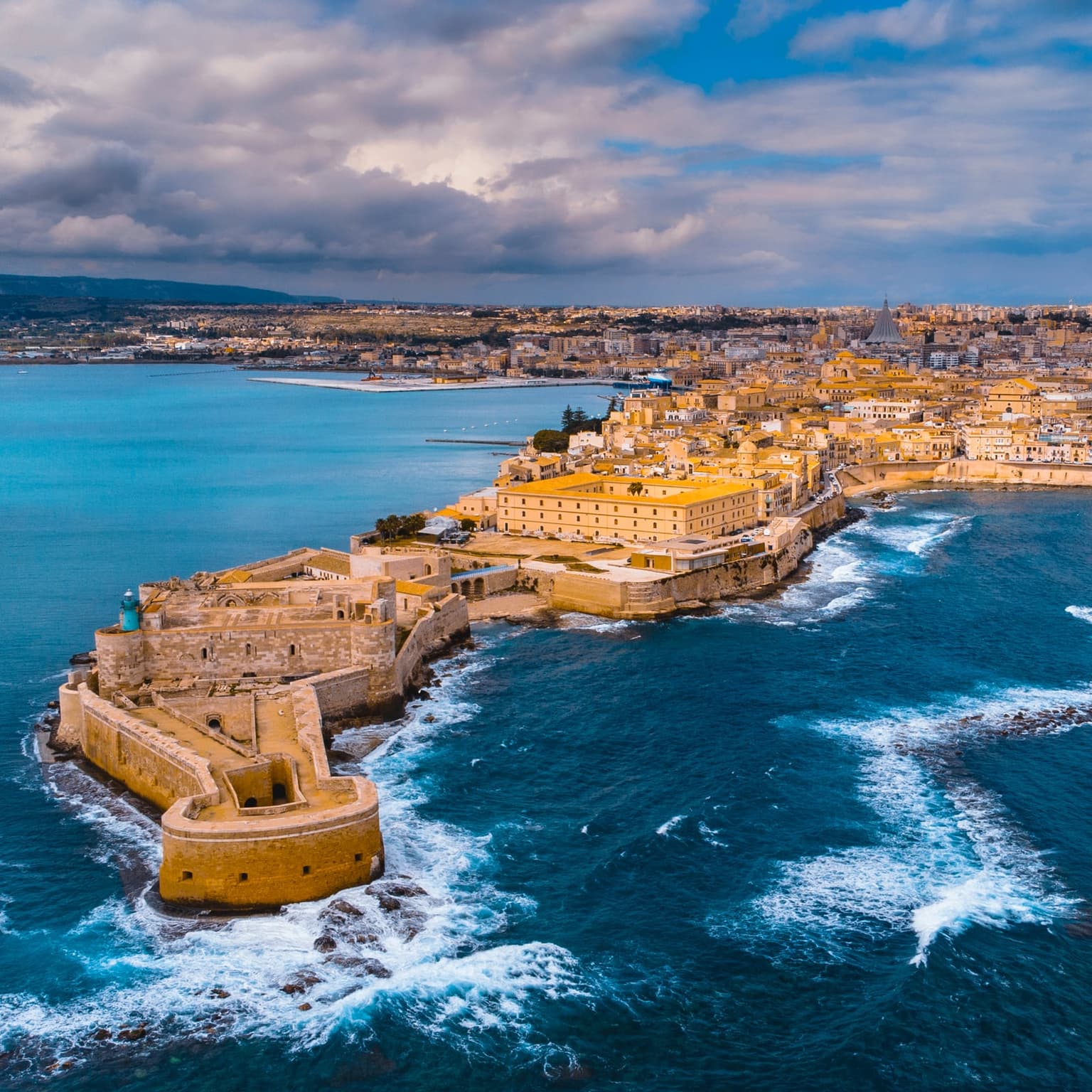 Aerial view of Castello Maniace at Ortigia's tip, waves breaking against its walls on three sides