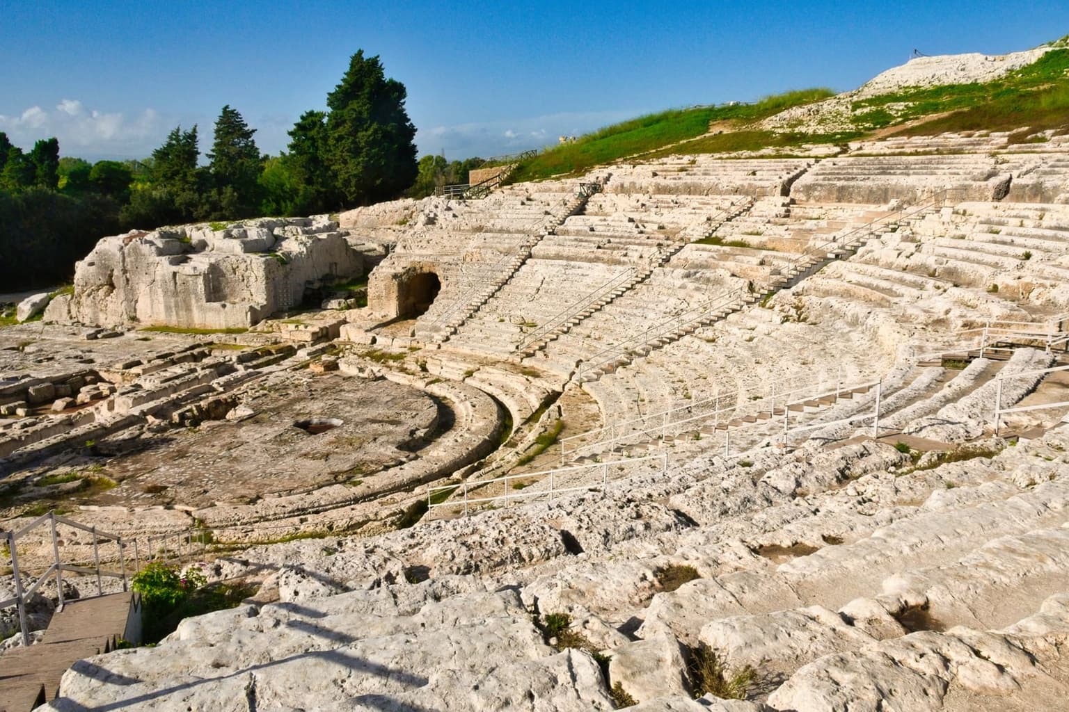 The Greek theater's stone tiers cut into the hillside, the city and the sea visible beyond
