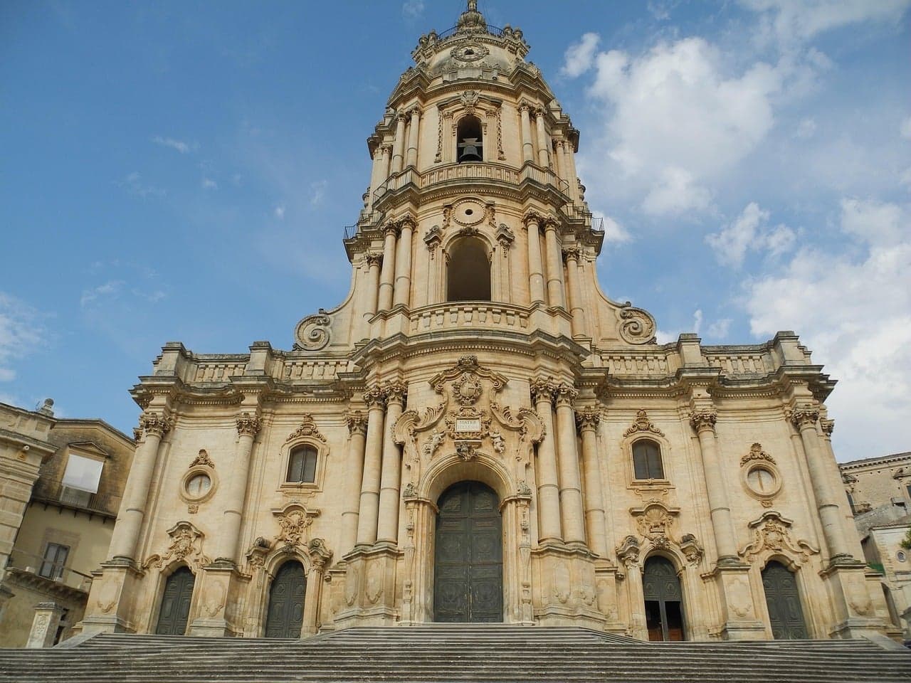 The Duomo di San Giorgio in Modica, its honey-colored baroque tower rising in tiers, the same stone and style as Ortigia's own lanes