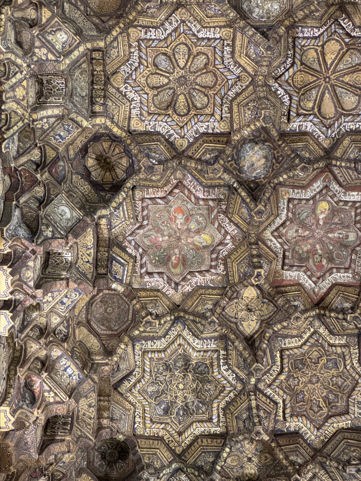 The Cappella Palatina's wooden muqarnas ceiling seen from below, star-shaped honeycomb panels painted in gold, red and blue in a Fatimid-style geometric pattern