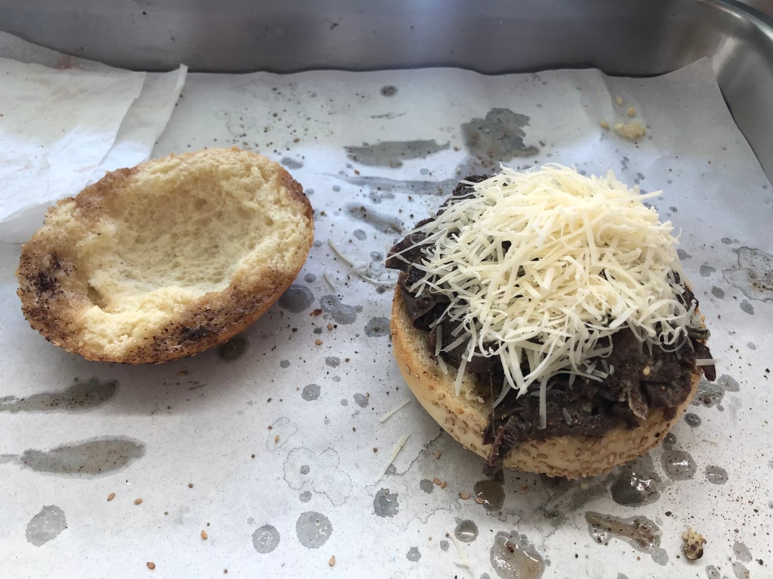 A pane con la milza roll split open on a food-stall counter, the bottom half piled with sautéed spleen and topped with a mound of freshly grated caciocavallo