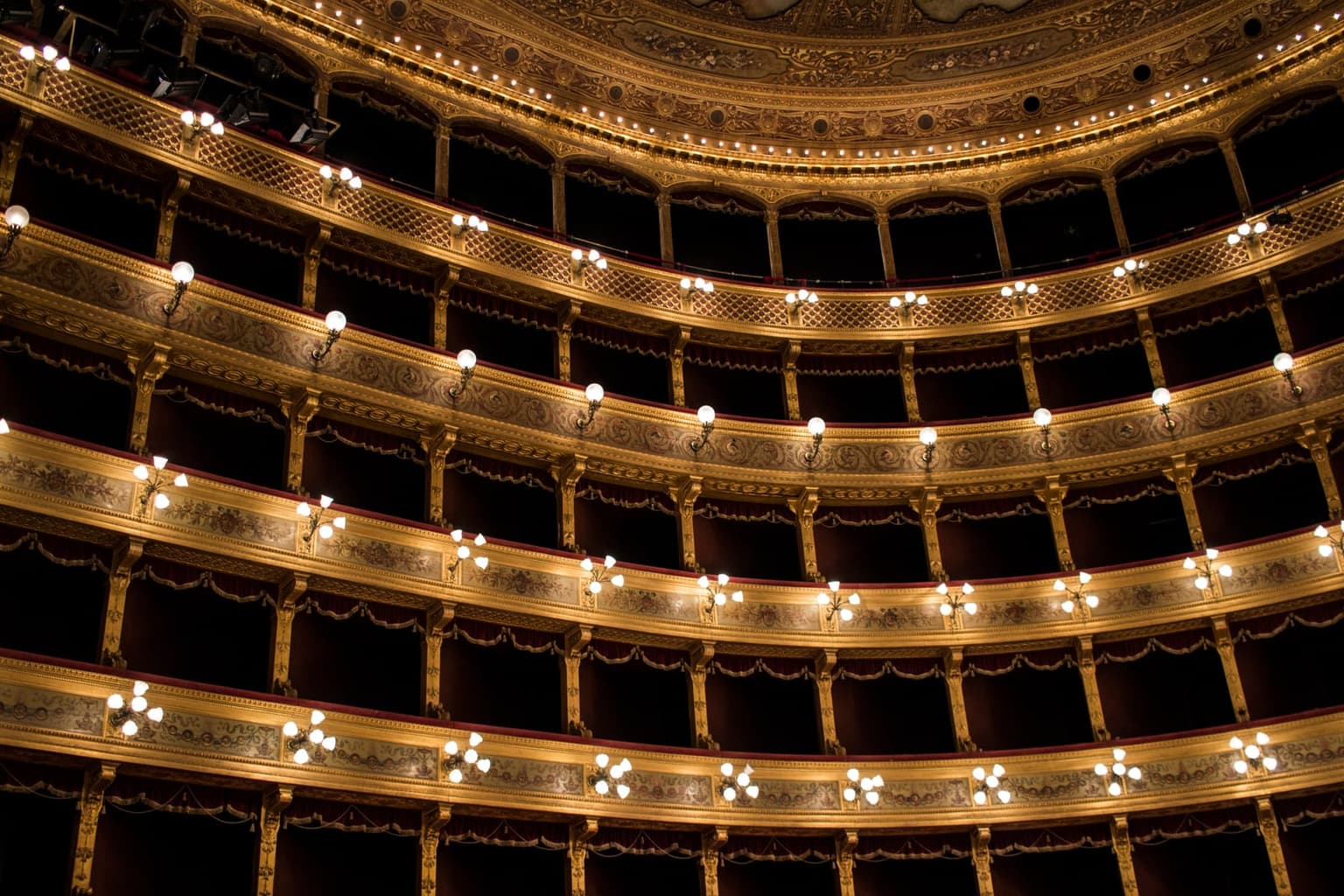 Teatro Massimo's gilded horseshoe-shaped auditorium seen from a box, tiers of empty balconies curving away under an ornate painted ceiling