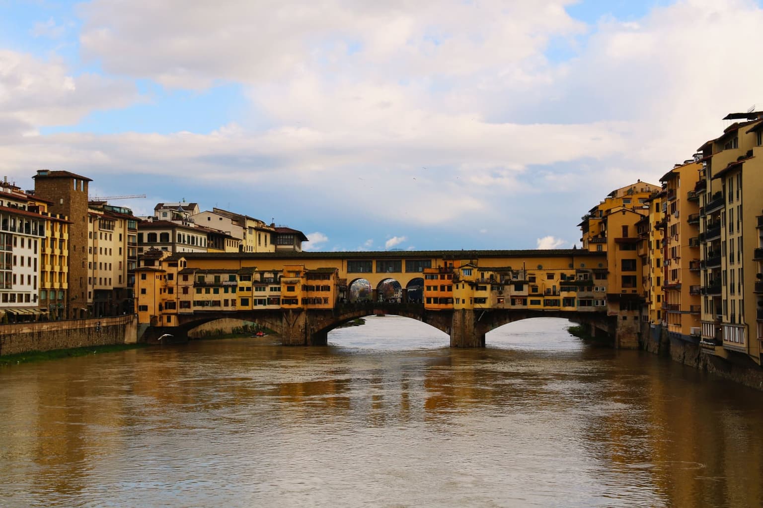 Ponte Vecchio over the high, brown Arno, its three stone arches topped with small ochre shops and a covered corridor