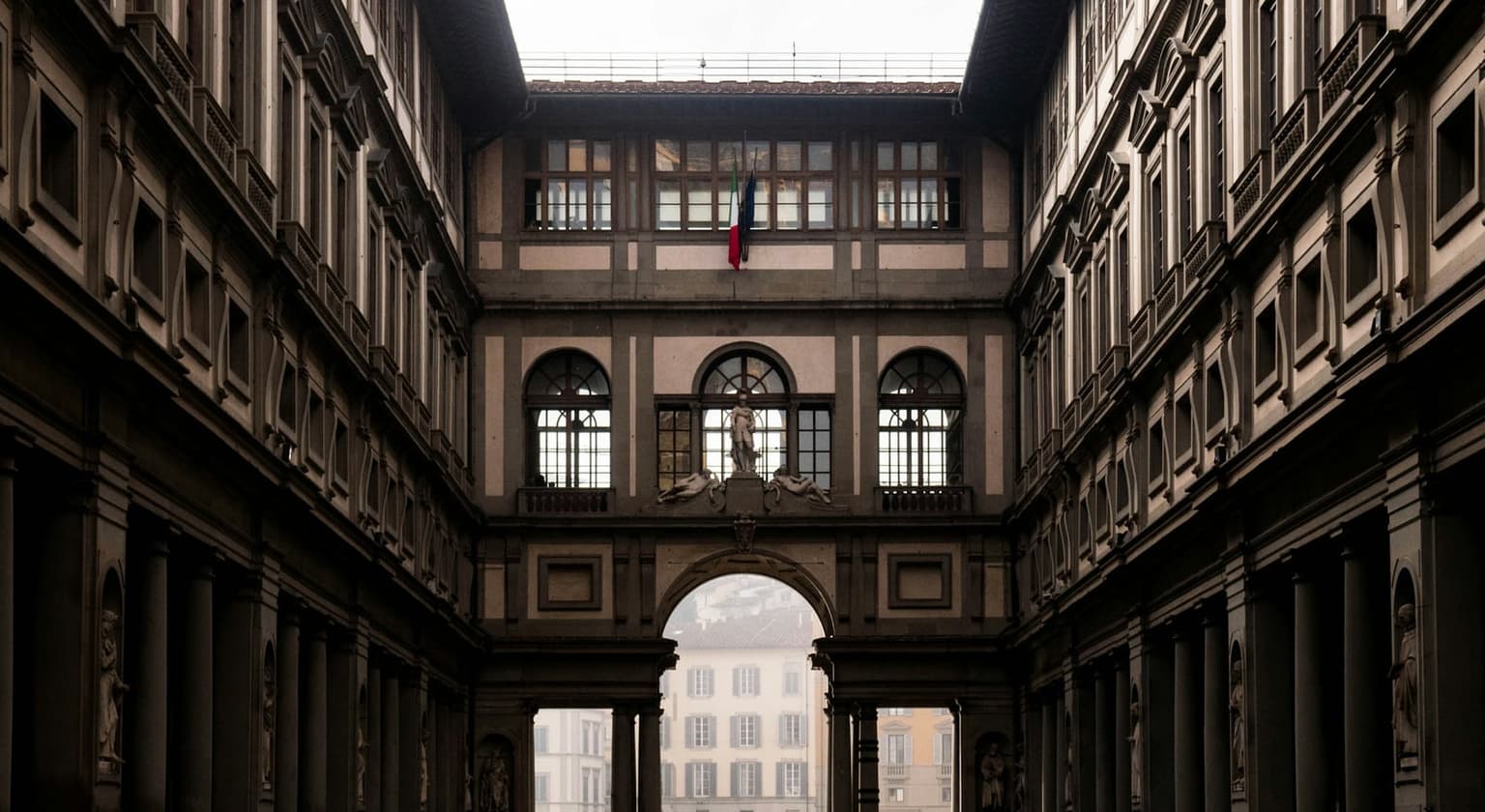 The Uffizi's long, narrow courtyard between two matching stone wings, ending in an arched loggia that opens toward the river