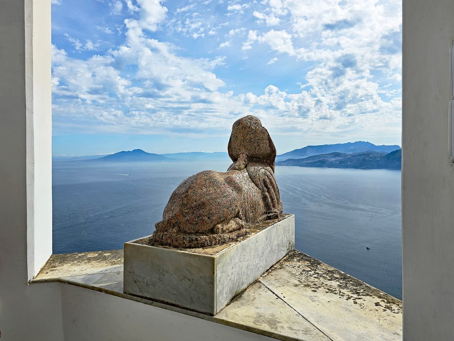 The red granite sphinx of Villa San Michele in Anacapri on its marble pedestal at the parapet, gazing out over the Bay of Naples toward Vesuvius and the Sorrento peninsula
