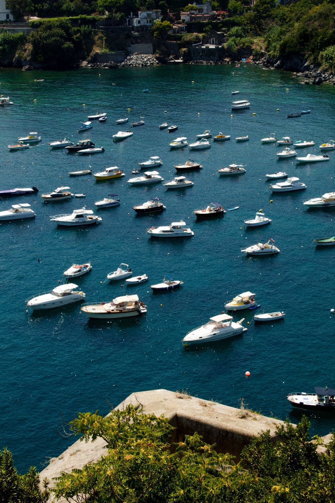 Dozens of small boats at anchor in clear blue-green water off Ischia Ponte, seen from a bastion of the Castello Aragonese