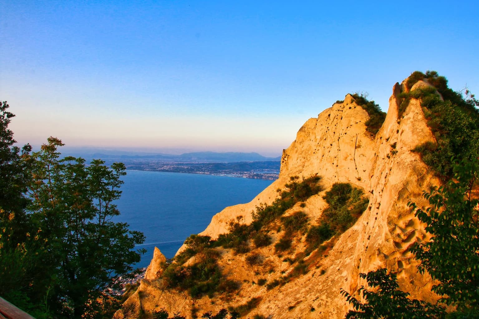 The pale tuff crags of Mount Epomeo's summit lit gold by the low sun, with the sea and the coast far below