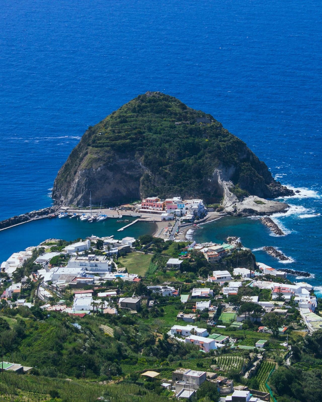 Sant'Angelo on Ischia's south coast from the hillside, a green islet joined to the village by a narrow sandy isthmus, with a small harbor on one side and a beach on the other