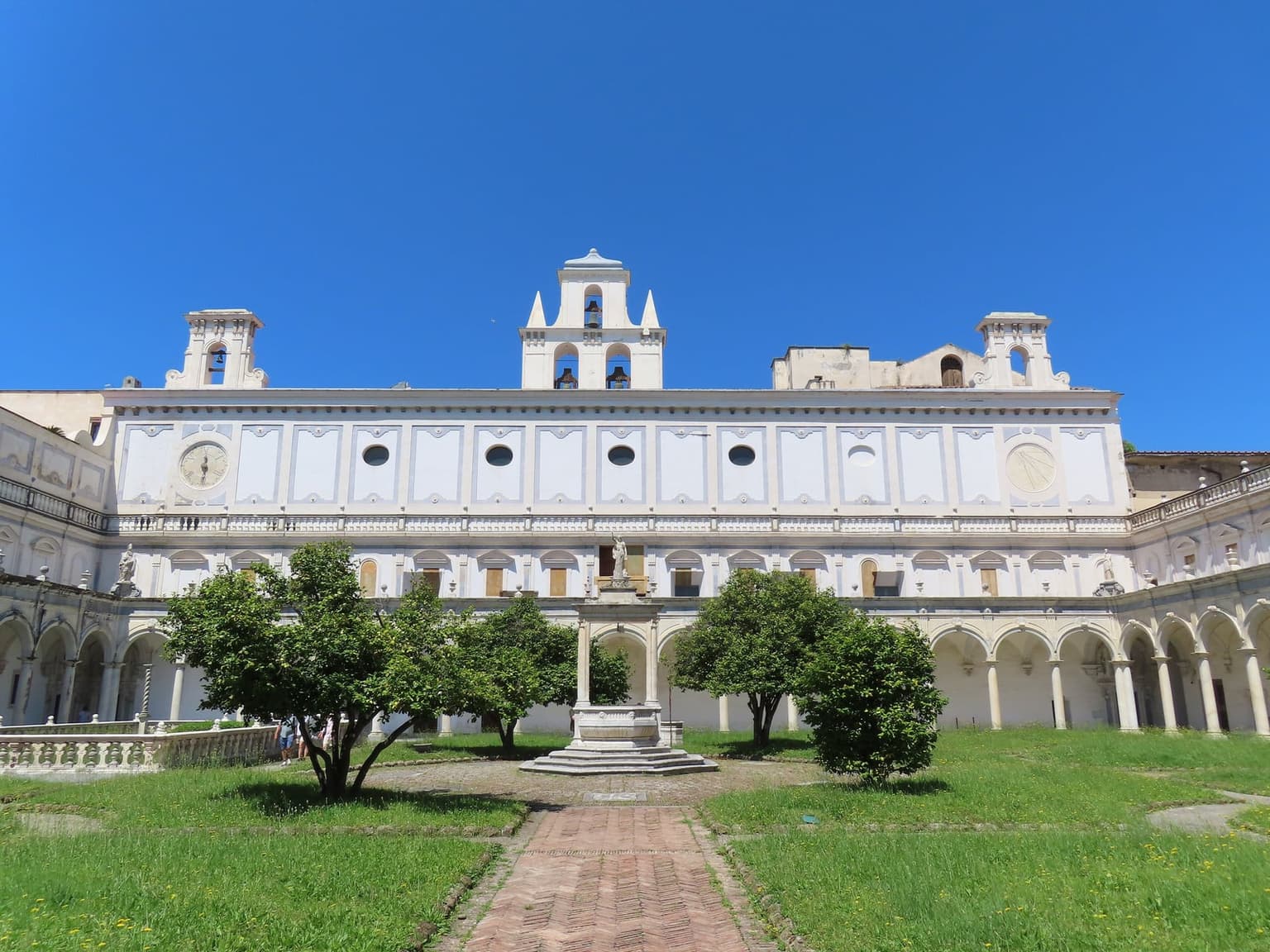 The great cloister of the Certosa di San Martino, a white arcaded courtyard with a marble well at its center