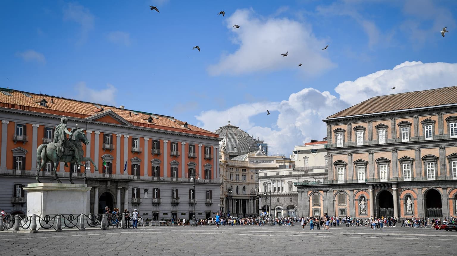 Piazza del Plebiscito by day, with an equestrian statue, the Palazzo Reale facade on the right and crowds crossing the square
