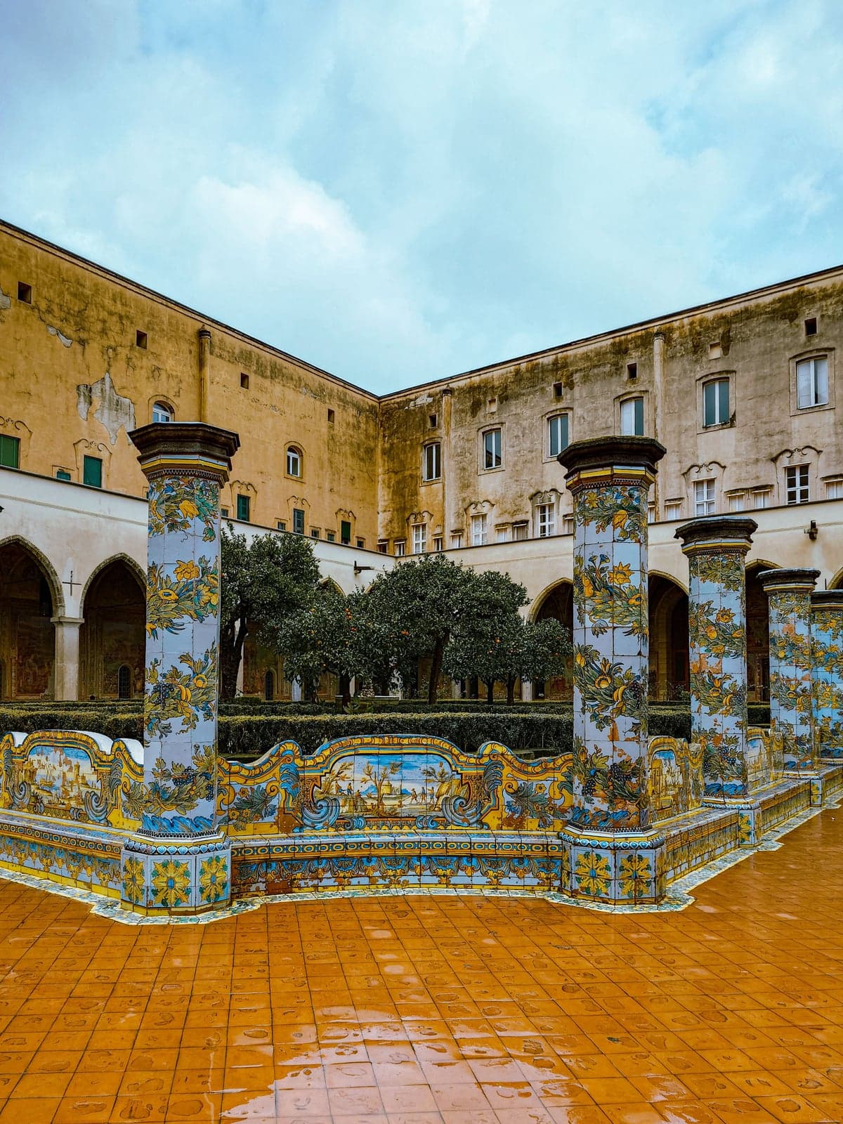 Santa Chiara's majolica cloister, with pillars and benches covered in hand-painted yellow and blue tiles and orange trees behind