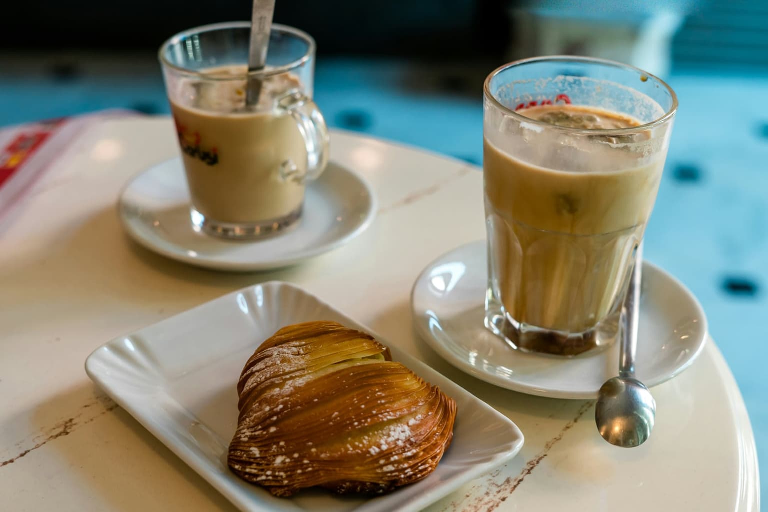 A sfogliatella riccia dusted with powdered sugar, its thin pastry layers fanned in ridges, next to two glasses of coffee