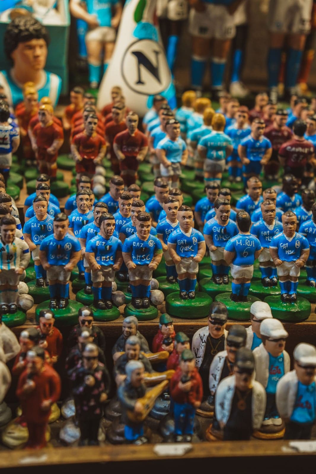 Handmade figurines of Napoli football players crowded on a stall, with a larger Maradona figure behind them