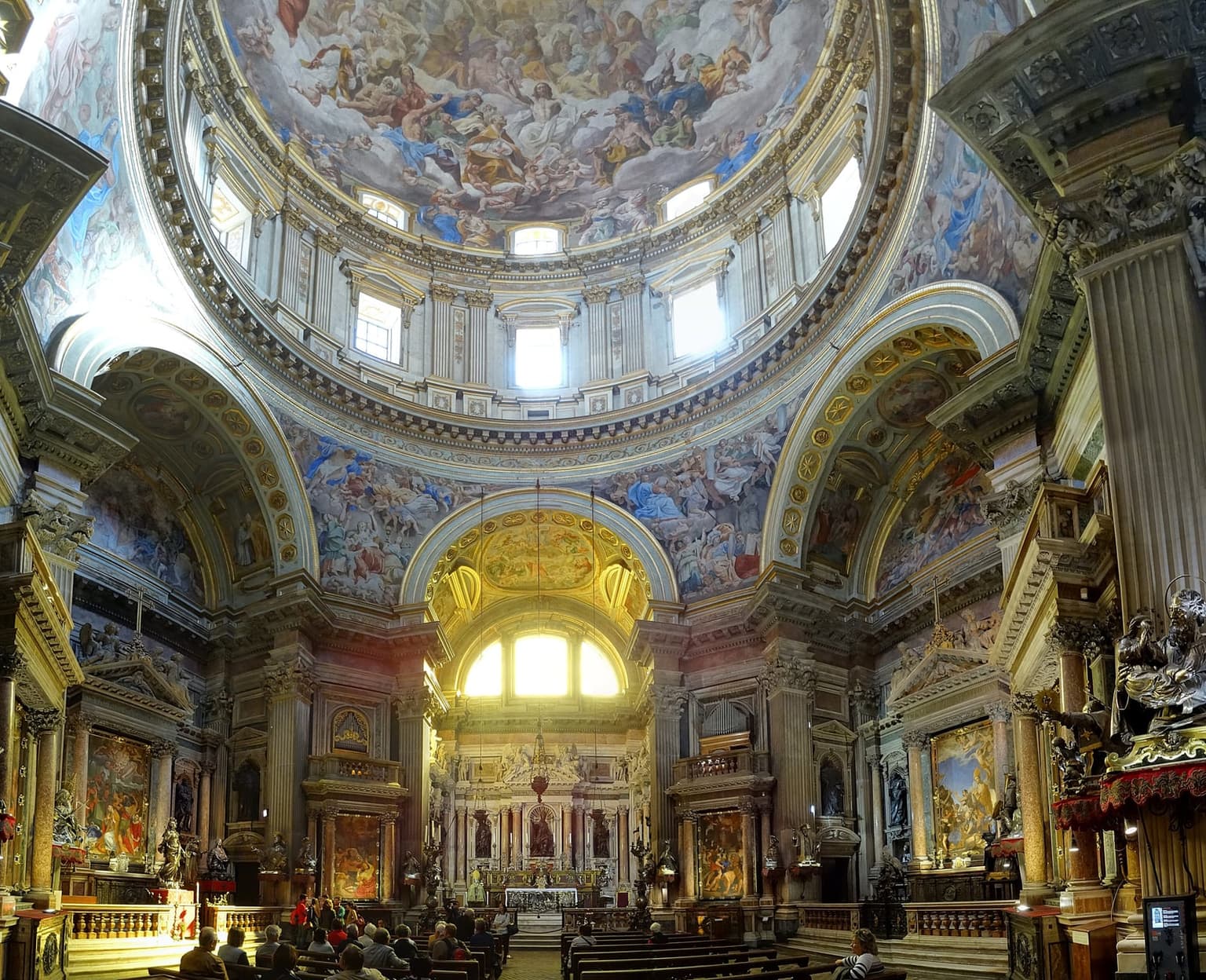 The Chapel of the Treasure of San Gennaro inside the Duomo, with a frescoed dome, gilded arches and silver statues, and visitors seated facing the high altar