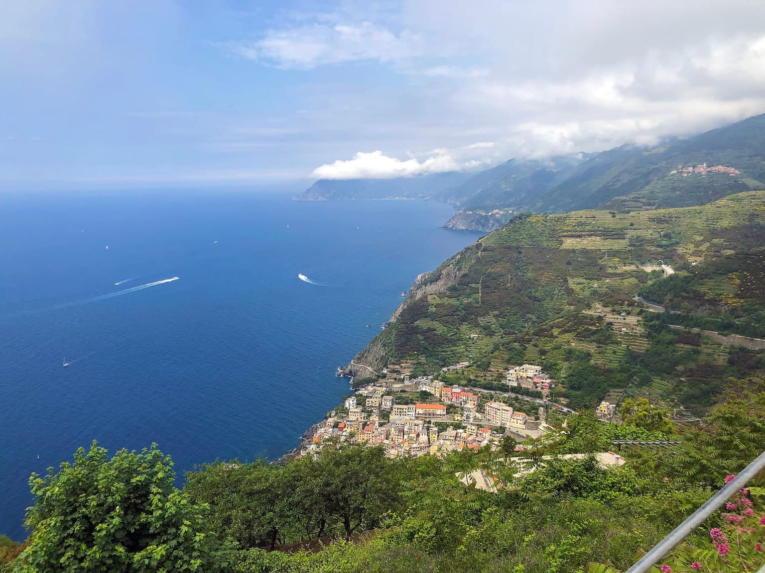Riomaggiore and its terraced slopes seen from the Montenero sanctuary above the coast, with boats on the sea below.