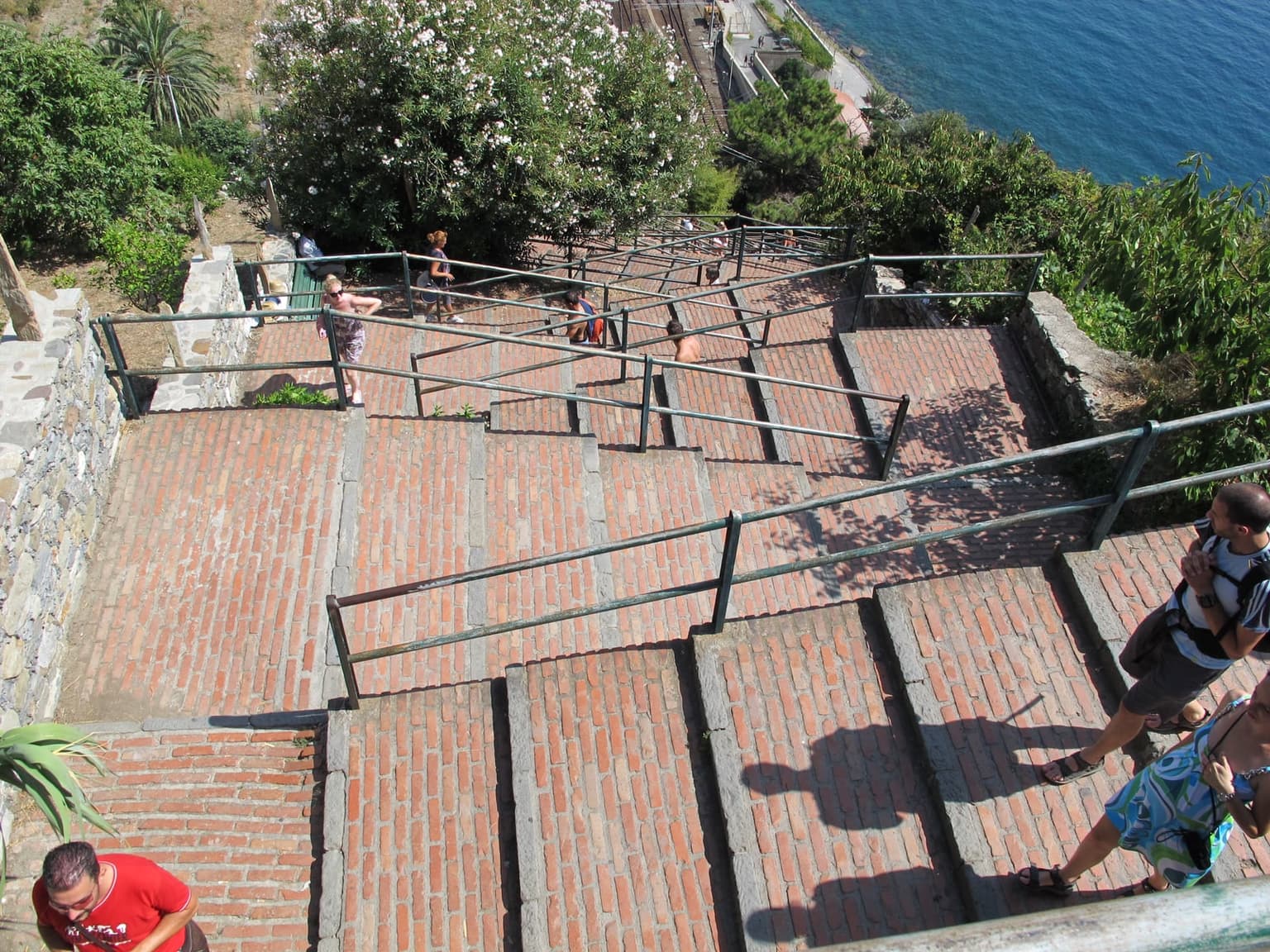 The Lardarina's brick stair flights zigzag down toward Corniglia station, with hikers on the steps.