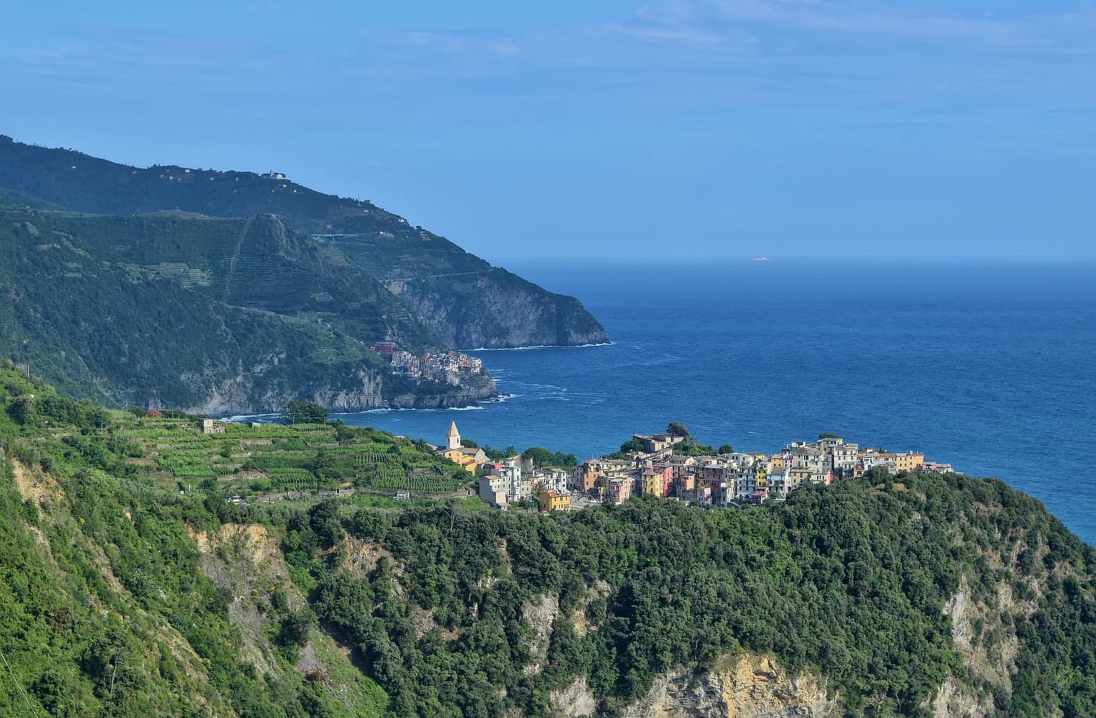 Corniglia on its headland above the sea, seen from the coastal path, with terraced vineyards beside the village.