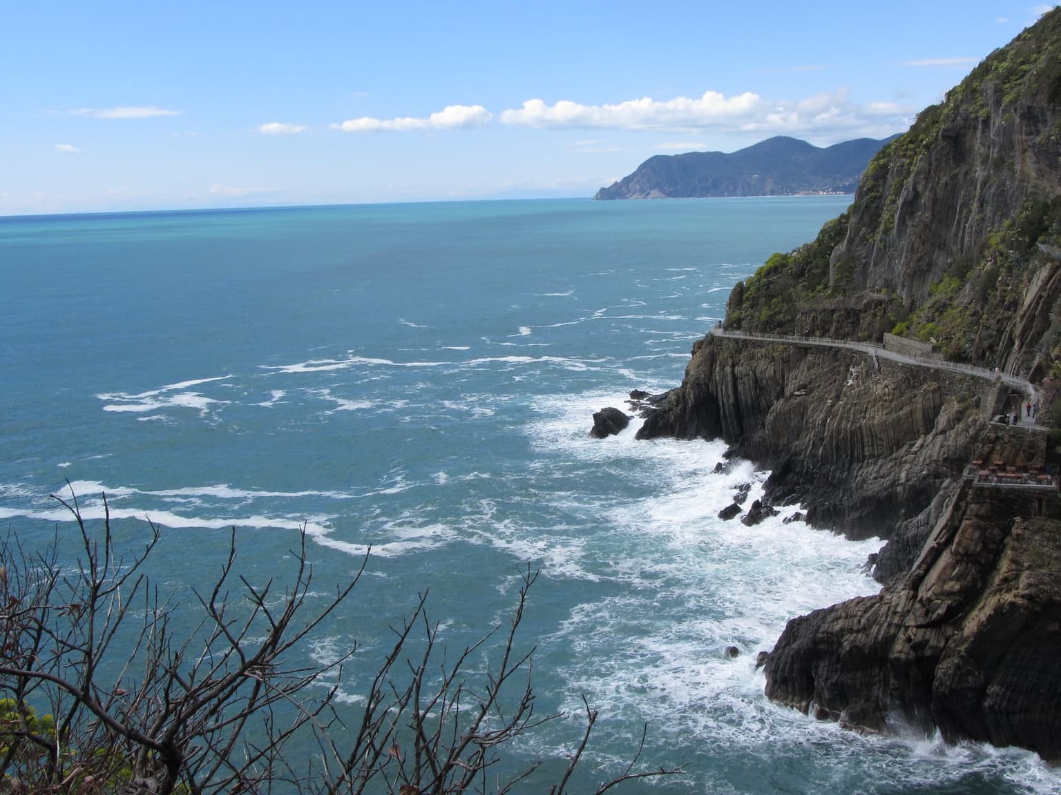 The Via dell'Amore walkway cut into a sheer cliff above breaking surf, with open sea beside it.