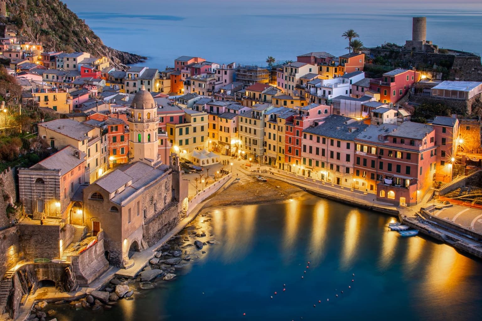 Vernazza's harbor and tower at dusk, with the street lights coming on along the waterfront