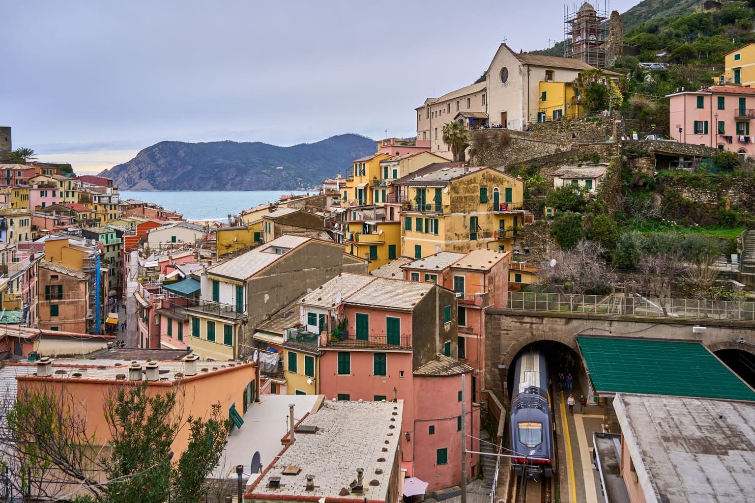 A train pulling out of a tunnel at a station among the houses of a Cinque Terre village